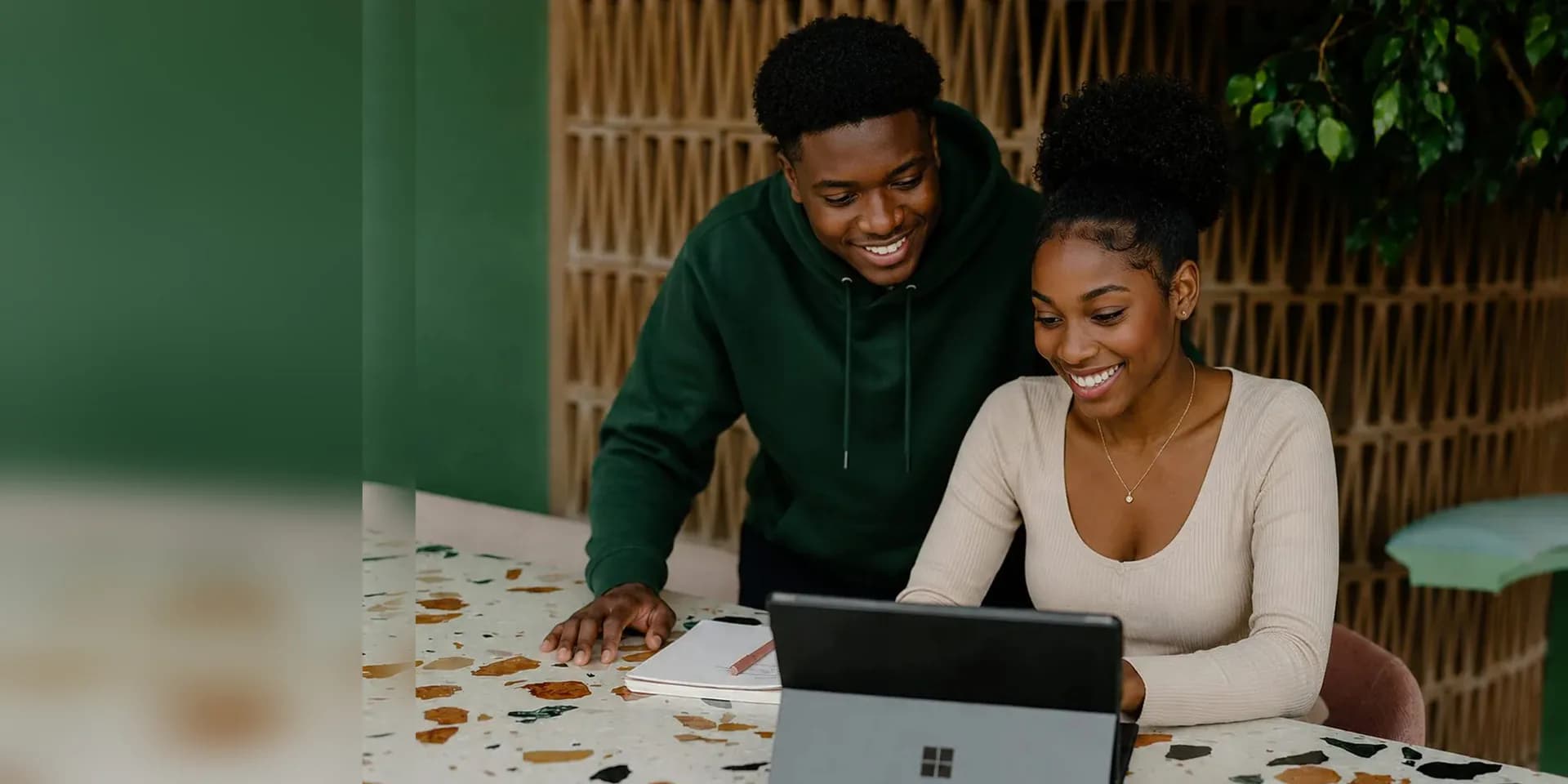 Un étudiant et une étudiante, souriants, regardent ensemble une tablette posée sur une table.